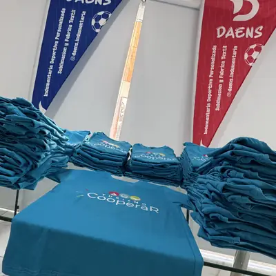 Remeras celestes de Turismo Cooperar apiladas sobre una mesa